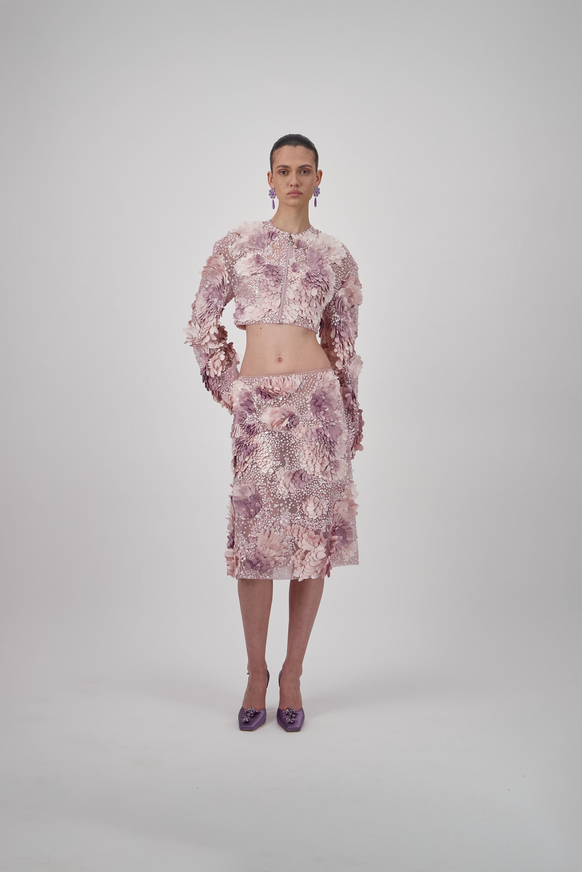 Embellished short skirt with intricate beadwork and three-dimensional floral appliqués in soft pink and mauve tones.