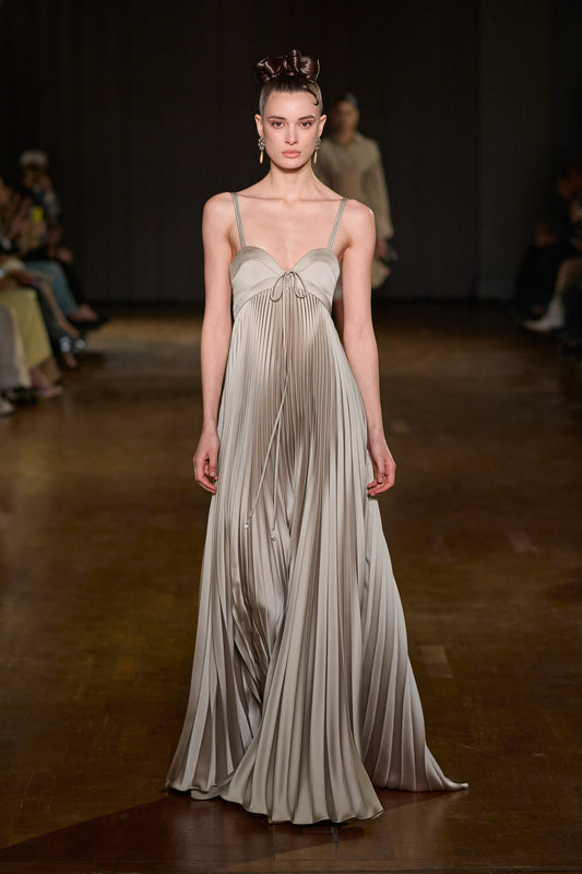 Floor-length pleated satin gown with structured bust, thin double straps, and delicate tie detailing at the neckline.