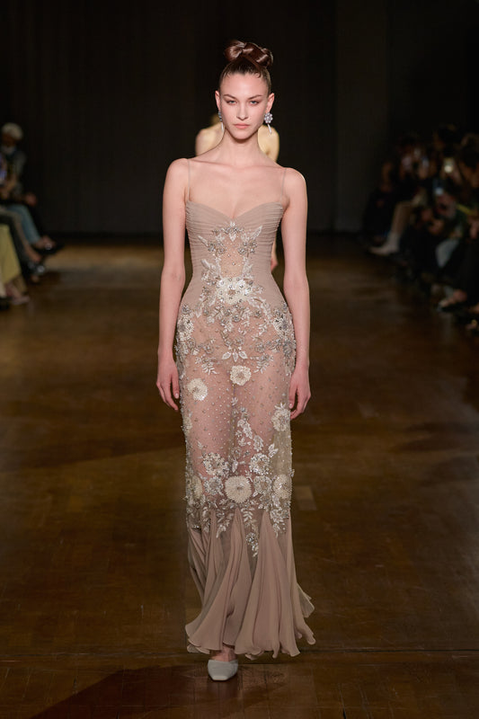 Nude tulle gown with draped bodice, thin straps, floral embroidery, crystal embellishments, and a fluid floor-length hem.