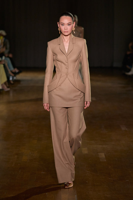 Taupe tailored jacket styled with a structured mini overskirt layered over matching wide-leg pants.