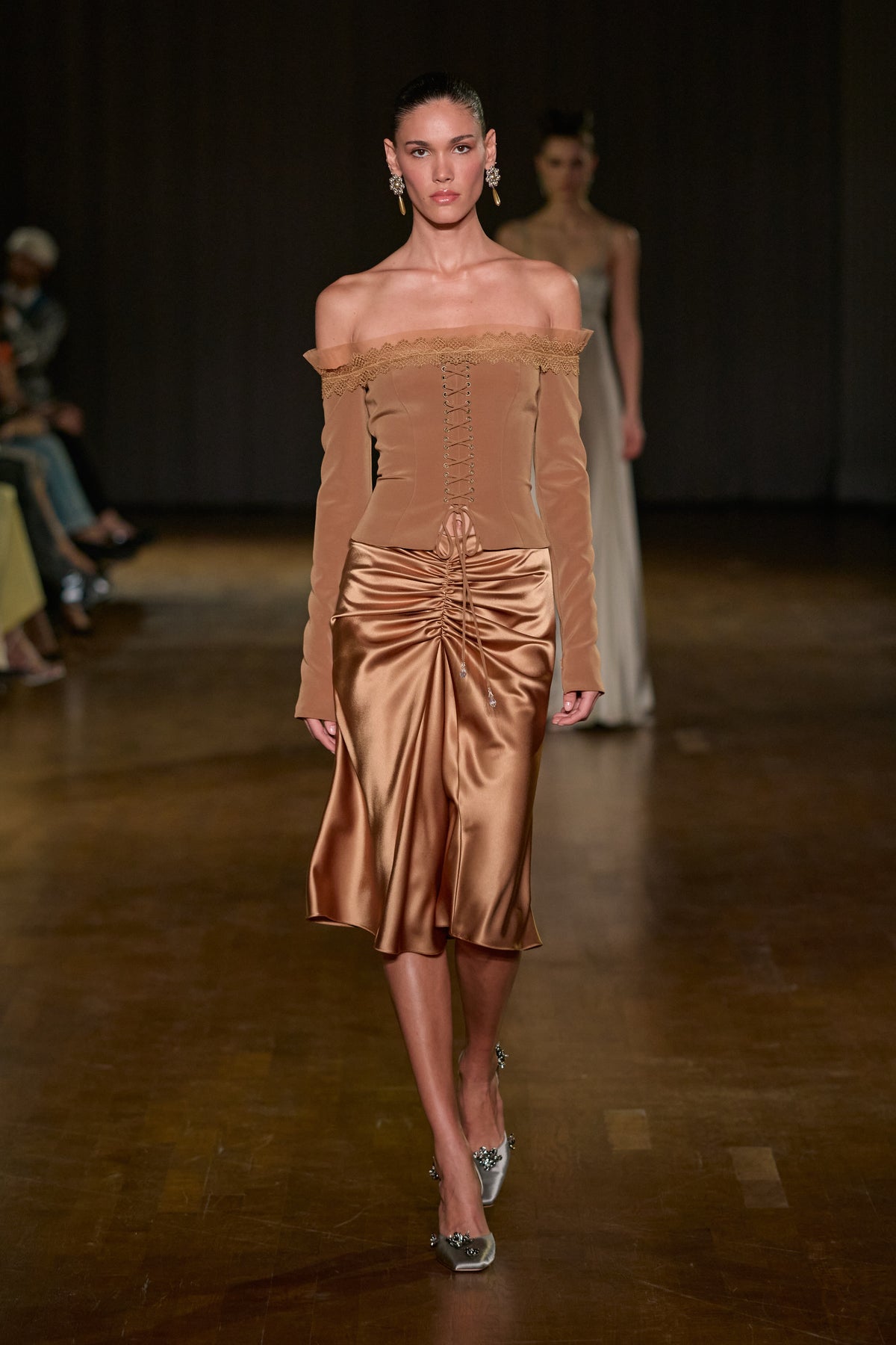 Brown off-shoulder lace-trimmed corset top paired with a bronze draped satin midi skirt with ruched detailing.