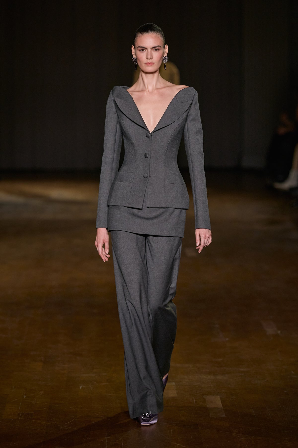 Grey tailored suit featuring a fitted deep-neckline jacket, structured mini overskirt and matching wide-leg trousers.