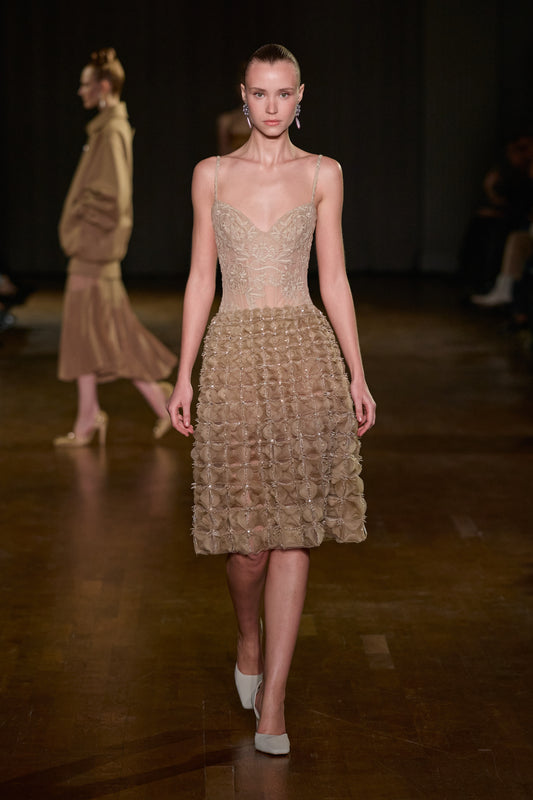 Beige sheer lace bodysuit with thin straps, paired with a voluminous textured midi skirt with delicate embellishments.