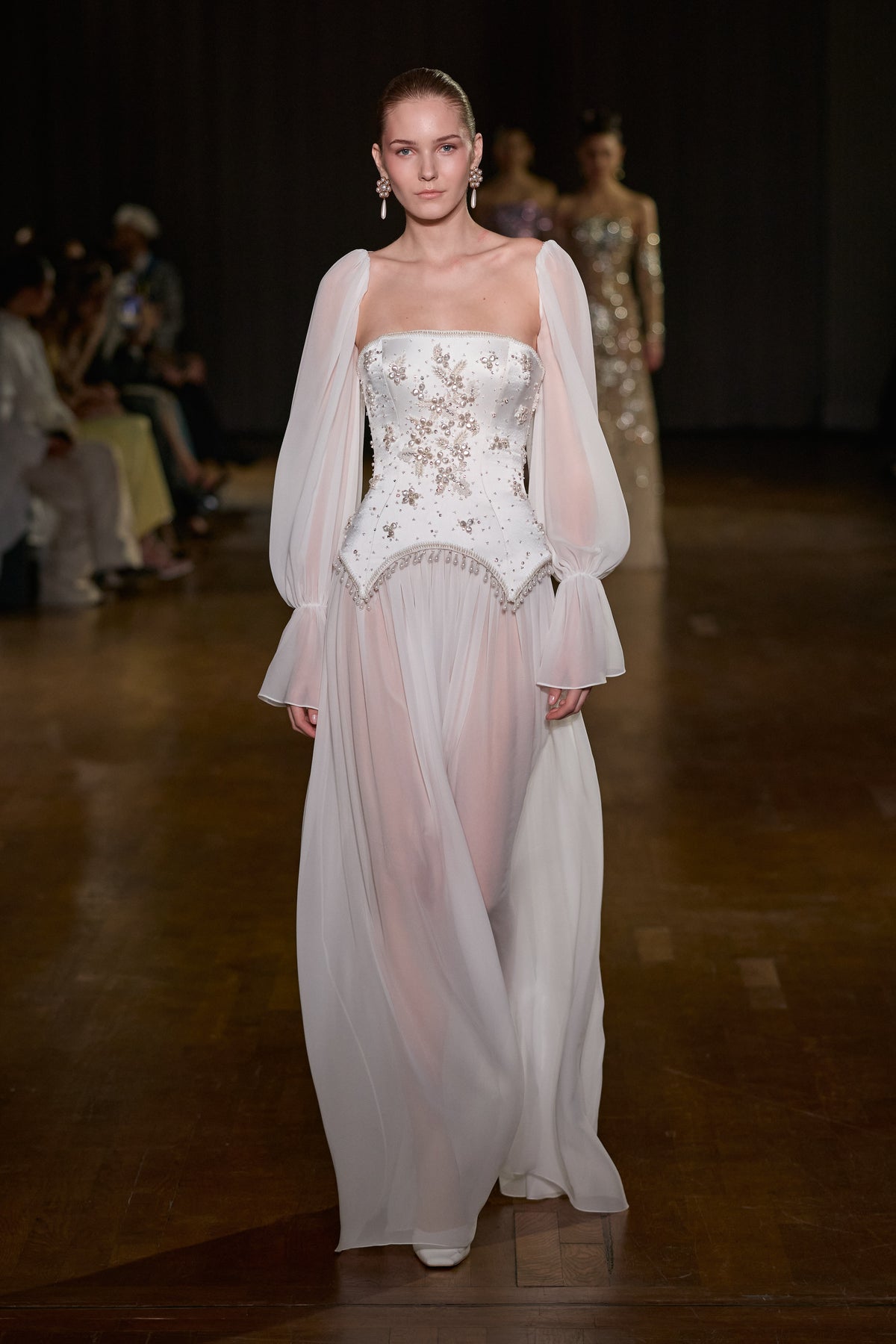 White floor-length chiffon gown with crystal-embellished structured bodice and sheer voluminous sleeves.