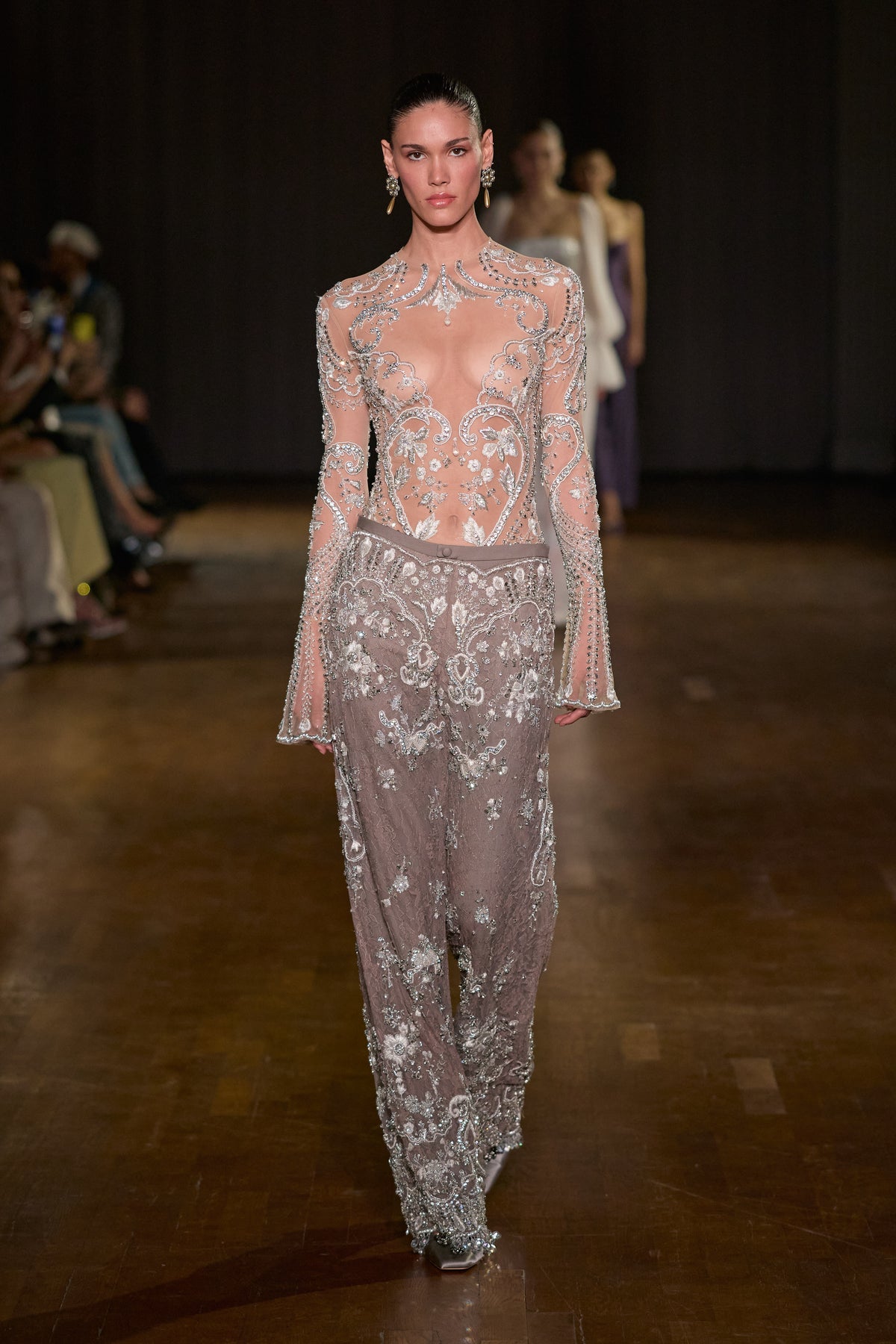 Sheer crystal-embellished bodysuit with flared sleeves, paired with embellished lace pants layered over wool.