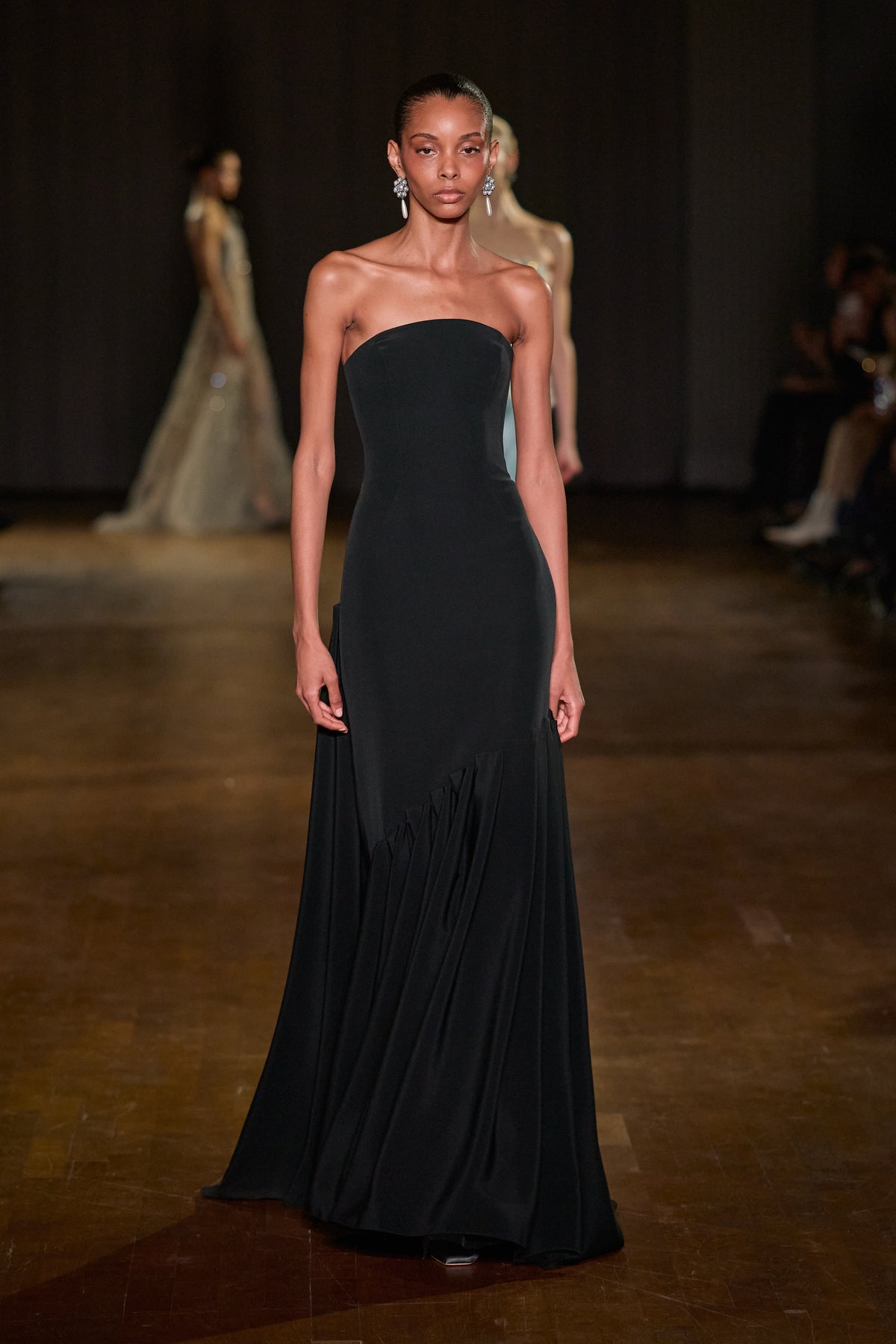Black strapless floor-length gown with a fitted silhouette and asymmetric draped skirt detailing.