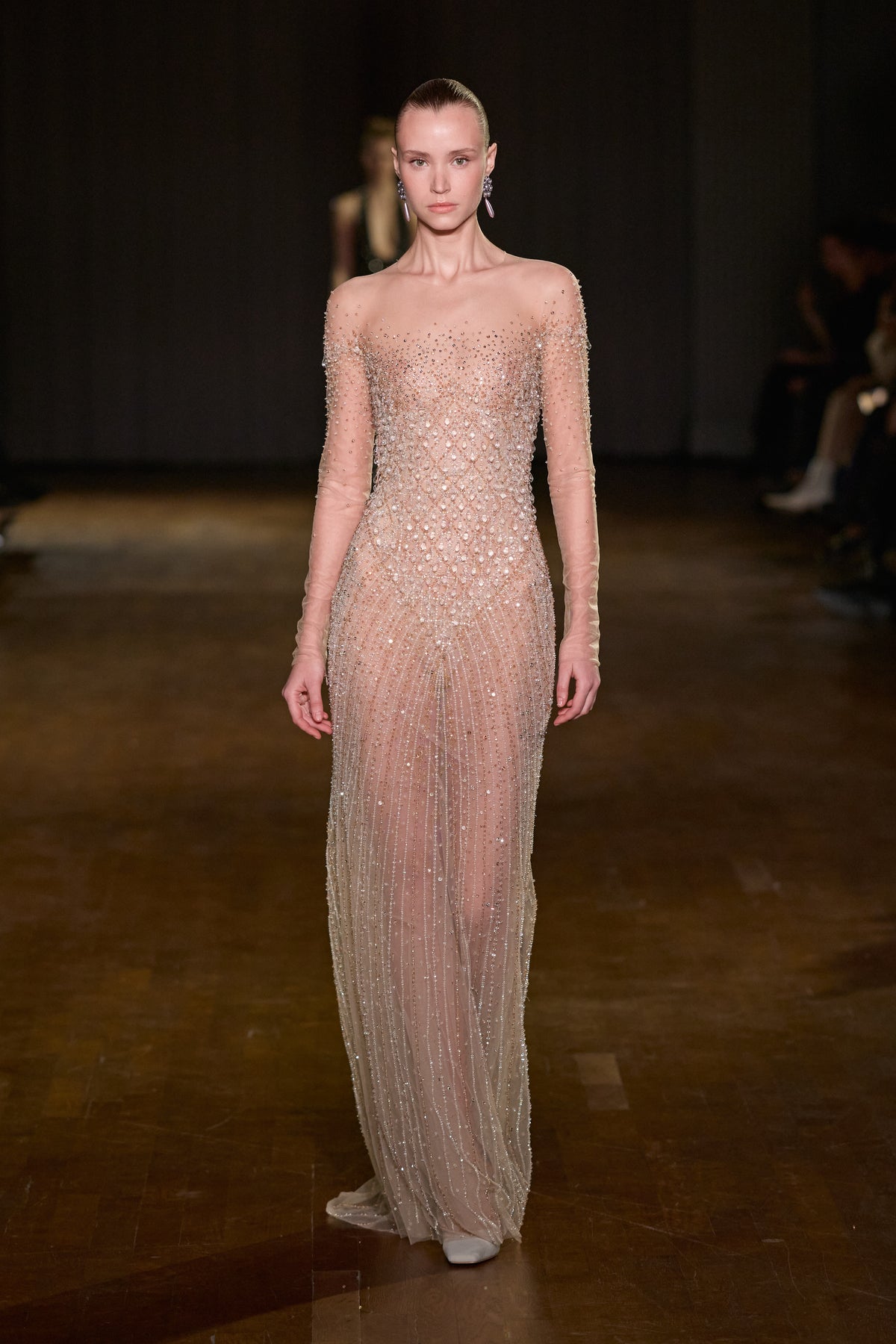Nude floor-length gown with sheer long sleeves and all-over crystal embellishments.