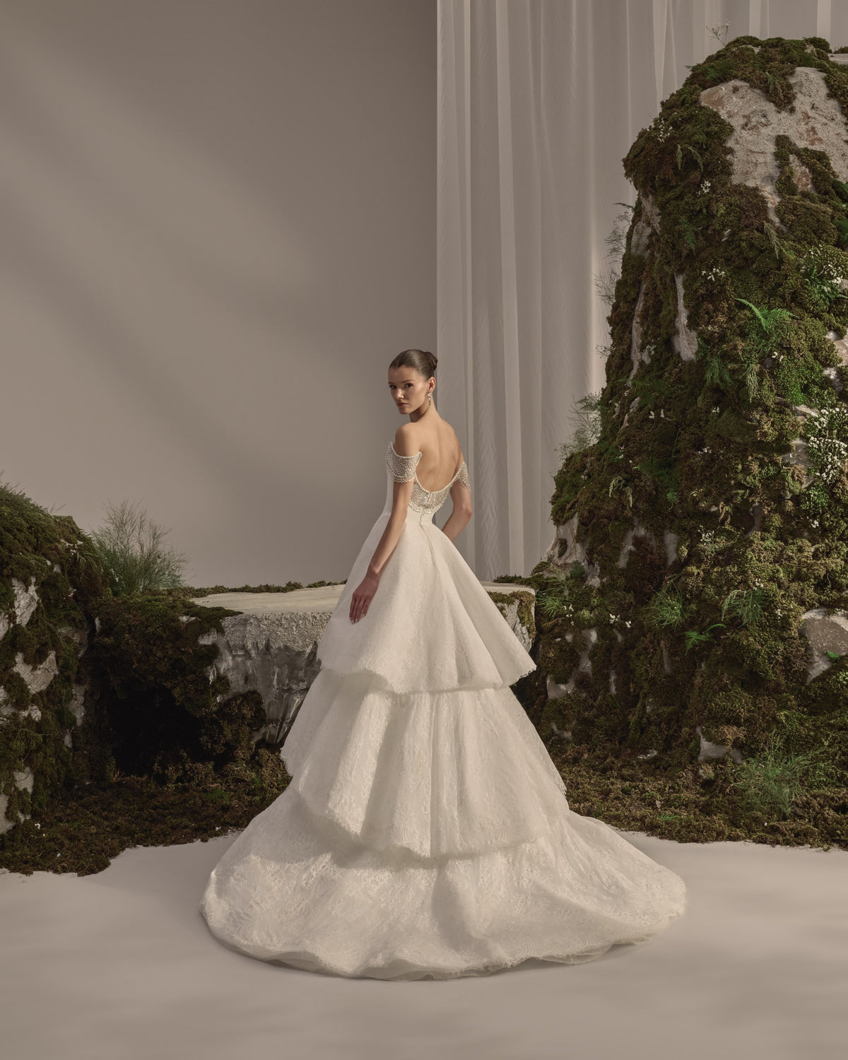 Off-shoulder bridal gown with an embellished draped neckline, fitted silhouette, voluminous lace overskirt and long sheer veil.